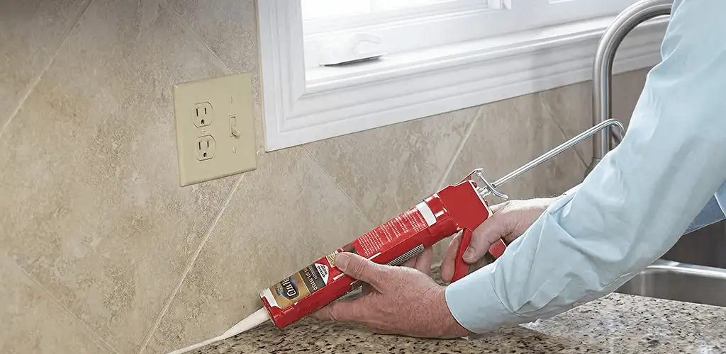 Handyman applying caulk along a kitchen backsplash and countertop seam in Phoenix, AZ